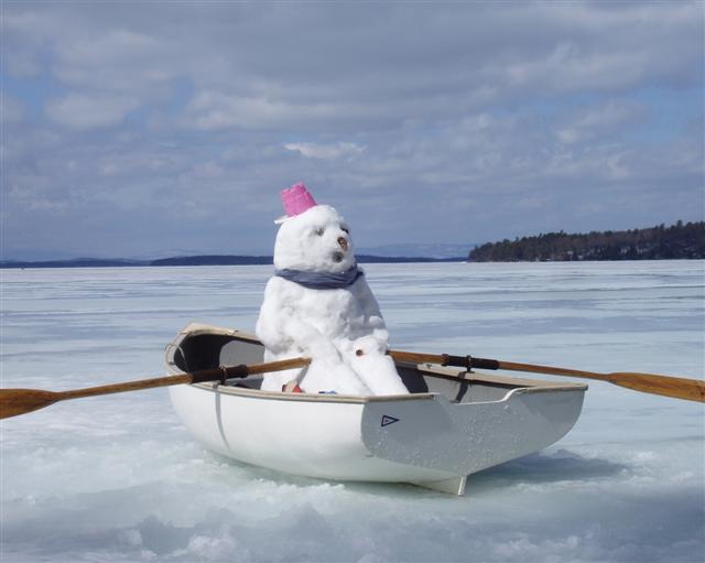 Snowman in a white boat with two brown paddles on the surface of frozen water.