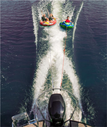 Boat with a TurboSwing ski tow bar attached pulling two tubes with people on them.
